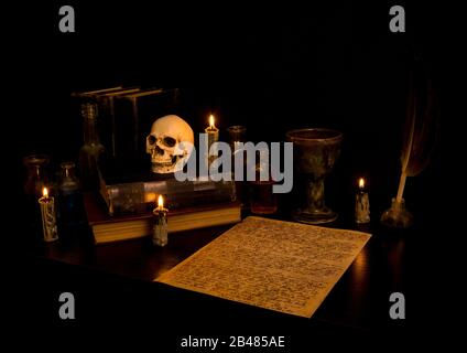 Bureau de l'assistant éclairé par une bougie. Crâne humain, vieux livres, un goblet, potion bouteilles. Papier parchemin avec écriture de canne à arcane. Stylo plume en inkwell. Banque D'Images