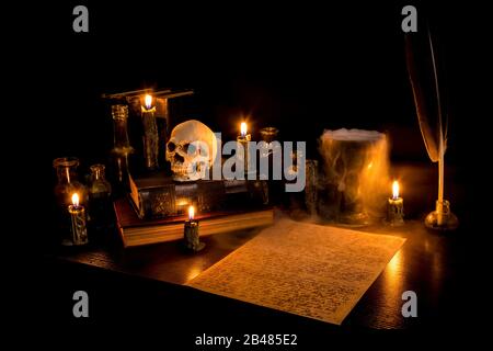 Bureau de l'assistant éclairé par une bougie. Crâne humain, vieux livres, un goblet, potion bouteilles. Le brouillard s'écoule du goblet sur du papier parchemin avec de l'écriture en arcane. Banque D'Images