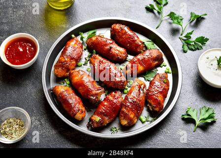 Ailes de poulet grillé enveloppées de bacon sur fond de pierre sombre. En-cas savoureux à base de viande de poulet, de bacon dans une sauce douce, aigre, salée et épicée. C Banque D'Images