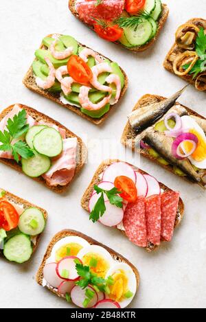 Ensemble de différents sandwichs avec viande, légumes, fruits de mer. Assortiment de sandwichs ouverts sur fond de pierre légère. En-cas savoureux et sains. Vue sur le dessus, plat Banque D'Images