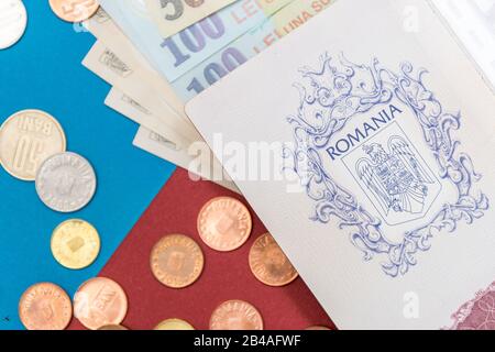 Concept roumain. Le passeport roumain et les billets/pièces roumains sur fond bleu et rouge. Colosse de Passeport roumain et de monnaie roumaine Banque D'Images