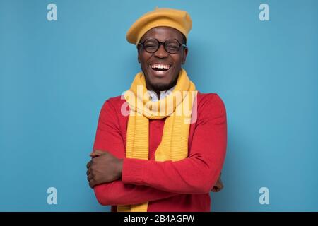 Bel homme noir afro-américain en pull rouge, chapeau jaune et écharpe, lunettes souriant regardant l'appareil photo en confiance. Émotion faciale positive. Banque D'Images