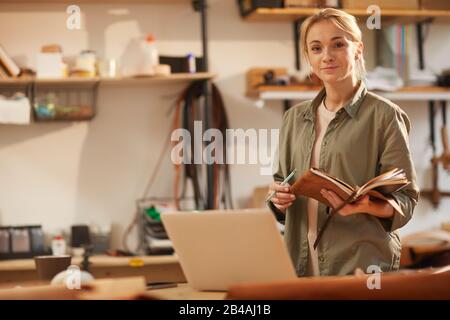 Portrait horizontal d'une jeune femme séduisante portant une tenue décontractée debout sur une table avec un ordinateur portable sur celle-ci tenant des ordinateurs portables regardant l'appareil photo Banque D'Images