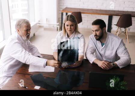 Un groupe de trois médecins adultes et jeunes discute des rayons X de la poitrine Banque D'Images