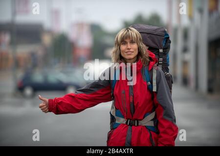 Femme vêtue de tissu rouge vif voyage par itchranking. Les voitures non reconnaissables sont à l'arrière-plan. La femme a un sac à dos sur elle-même. Banque D'Images