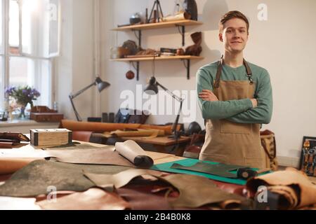 Portrait horizontal moyen long de l'artisan jeune et confiant portant un tablier debout avec des bras croisés regardant l'appareil photo, espace de copie Banque D'Images