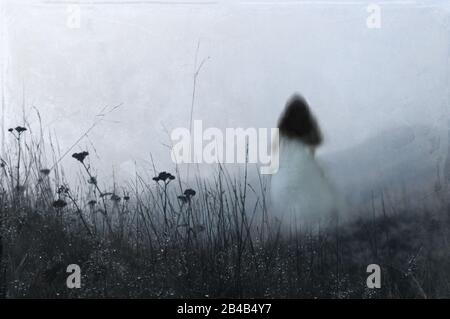 Une femme fantomatique bleutée et hors de la mise au point portant une robe blanche, s'éloignant de l'appareil photo. Une journée d'hivers brumeux dans la campagne. Avec un artiste Banque D'Images