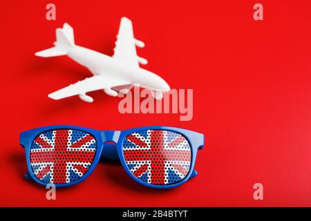 Un avion de passagers blanc vole dans des lunettes de soleil avec le drapeau du Royaume-Uni, sur un fond rouge. Le concept de voyage en Angleterre. Espace libre. Il Banque D'Images