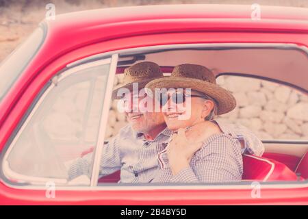 un beau couple d'adultes se cahote et adore l'intérieur d'une vieille voiture rouge d'époque stationnée sur la route. sourires et plaisir de voyager ensemble. bonheur et style de vie pour les gens agréables. l'été et le voyage de vacances Banque D'Images