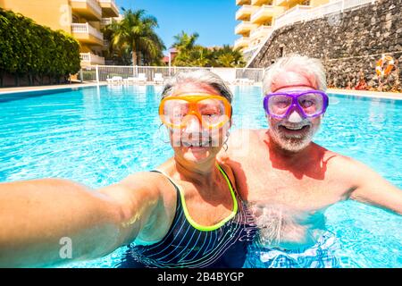 Joyeuses personnes âgées l'homme et la femme de haut niveau s'amusent ensemble dans la piscine d'été en prenant des photos de selfie avec des masques de plongée sur le visage pour des activités de loisirs en plein air drôles en vacances à l'hôtel Banque D'Images