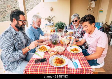 Les familles déjeuner en plein air ensemble sur une table rouge - les générations mixtes aiment et s'amusent avec des pâtes italiennes sur la terrasse à la maison - père grand-père et fils Banque D'Images