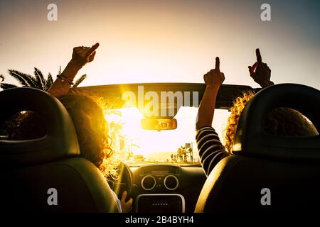 Les gens sont heureux de passer des vacances de voyage avec une voiture convertible donnant les mains et dansant pour les vacances d'été en mer - soleil à l'horizon et concept joyeux pour les femmes amis libres ensemble Banque D'Images