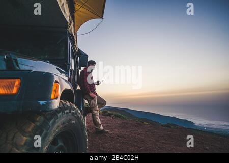 Voyageurs avec concept de voiture et de camping - homme solitaire utiliser le téléphone cellulaire pour se connecter à Internet en dehors de son véhicule - montagne et nature en plein air autour - profiter de la liberté et des vacances alternatives avec l'indépendance Banque D'Images