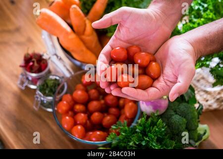 Légumes pour végétariens ou végétaliens ou des personnes saines de style de vie alimentaire - mélange de couleurs et de vitamines sur la table prêts à être mangés pour la perte de poids et la santé - homme caucasien prenant des tomates cerises Banque D'Images