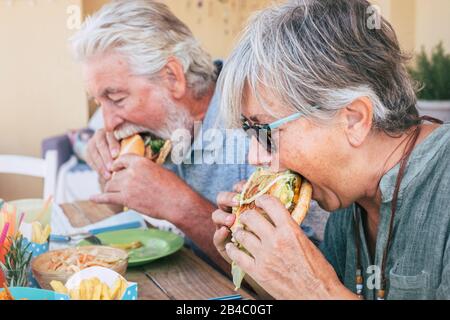 Les gens qui mangent des aliments indésirables de hamburgers - Couple de personnes âgées et de femmes avec des repas rapides déjeuner - gros plan sur les personnes âgées pas de mode de vie sain - sandwich savoureux plein de tout Banque D'Images