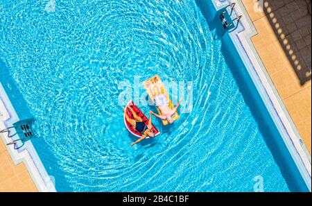 Vue aérienne verticale sur les personnes âgées couple profitant du style de vie à la retraite avec matelas gonflable lilas de couleur tendance sur une piscine d'eau bleue claire dans l'hôtel vacances d'été Banque D'Images