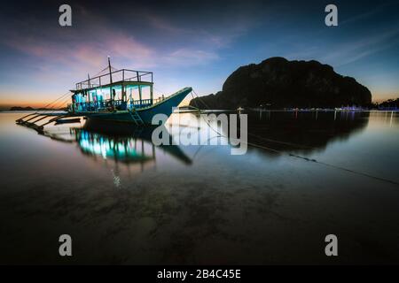 Baie tropicale de mer du port avec bateau banca en soirée. Heure bleue dans la lagune aux Philippines, Palawan, El Nido. Paysage rêveux tranquille, exposition longue. Banque D'Images