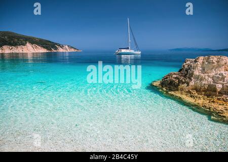 Beau lagon bleu azur avec catamaran à voile bateau au mouillage. Plage de galets blanc pur, quelques rochers dans la mer. Banque D'Images