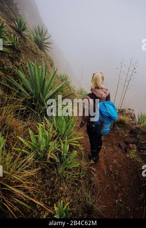 Voyageur féminin séjournant sur l'édouil du cratère inactif du volcan de cove au-dessus de la vallée verte brumeuse surcultivée avec des plantes yucca. Île de Santo Antao à Cabo Verde. Banque D'Images