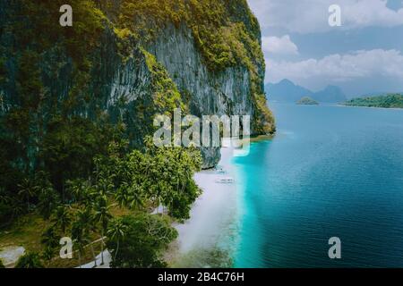 El Nido, Palawan, Philippines. Vue aérienne sur les bateaux touristiques arrivant à la plage tropicale d'Ipil sur l'île de Pinagbuyutan. Emplacement idyllique à distance avec eau turquoise bleu océan et palmiers. Banque D'Images