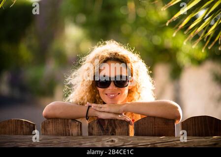 Portrait de la belle jeune femme blonde caucasienne gai gai regardant l'appareil photo avec des lumières du soleil en arrière-plan et défocused vert naturel en plein air - heureux concept de dame d'âge moyen Banque D'Images