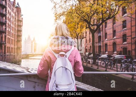 Vue arrière de la femme blonde adulte touristique avec sac à dos, profitant d'une belle scène de coucher de soleil sur le quartier historique de Speicherstadt à Hambourg, Allemagne, Europe. Banque D'Images