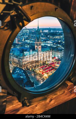 Vue de dessus du marché lumineux de Noël sur la place de la mairie à l'heure de l'avènement, Hambourg, Allemagne. Vue encadrée de la fenêtre de hublot. Banque D'Images