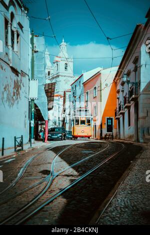 Paysage urbain d'été de Lisbonne. Le tramway rouge qui descend le long de la colline le long de vieilles maisons traditionnelles. Après-midi ensoleillé, rues étroites, route sinueuse pavée, vacances à Lisbonne. Banque D'Images