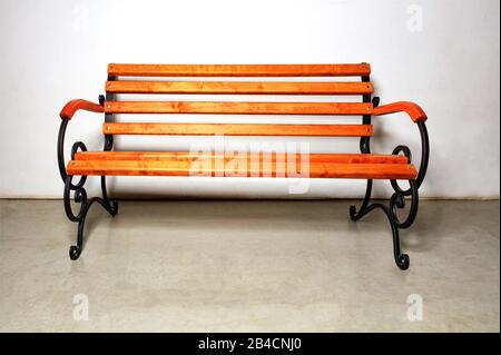 Banc en bois avec une base en métal forgé sur un mur blanc et un sol en béton. Banque D'Images