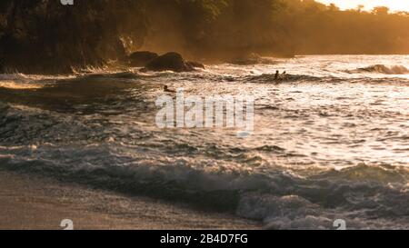 Les enfants surfent sur les vagues dans le coucher du soleil la lumière, Belle Baie Cristal, Nusa Penida, Bali Banque D'Images