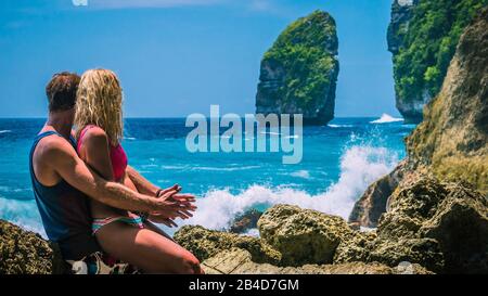 Couple devant le Rocher et regarder D'Énormes vagues frapper la Côte de Tembeling à Nusa Penida Island, Bali Indonésie. Banque D'Images