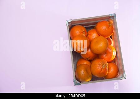 Beaucoup de tangerines dans une boîte en bois sur un fond rose Banque D'Images