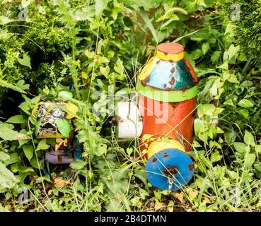 Un poteau incendie dans les mauvaises herbes est transformé en œuvre d'art avec une sculpture d'art de chien en métal placée à côté. Banque D'Images