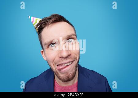 Drôle jeune homme avec une expression faciale folle debout devant l'appareil photo contre fond bleu tout en se amusant Banque D'Images