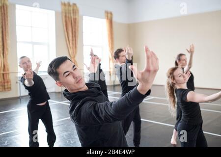 Jeune homme de handsome avec des bras étirés faisant un des exercices de danse sur fond de ses camarades de classe en studio Banque D'Images