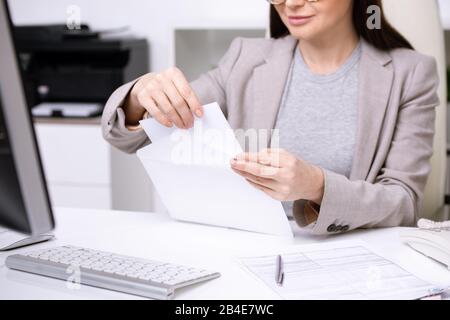 Mains de la jeune femme d'affaires ou banquier mettant du papier plié dans l'enveloppe blanche avant d'envoyer le document à l'un des clients Banque D'Images