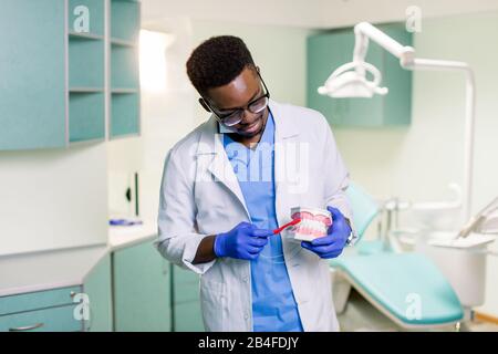 Un dentiste afro-américain montre comment brosser les dents avec une brosse à dents à l'aide de mâchoires artificielles. Banque D'Images