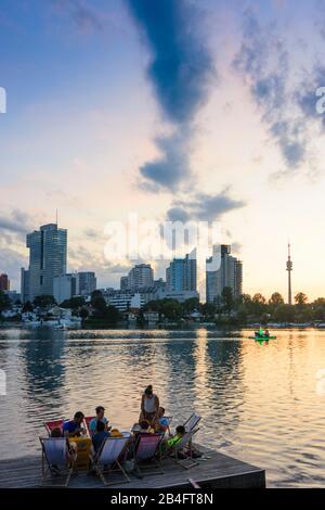 Wien / Vienne, lac oxbow rivière Alte Donau (Vieux Danube), coucher de soleil, Donaucity, Tour IZD, plate-forme en bois, transat, gens, restaurant, bateau en 22. Donaustadt, Wien, Autriche Banque D'Images