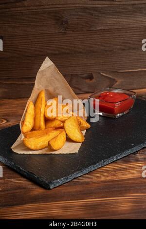 Pommes de terre rustiques avec vaisselle en ketchup ardoise, pierre noire sur fond en bois. Vertical. Gros plan. Banque D'Images