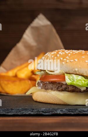 Hamburger sur les ustensiles en ardoise à côté des pommes de terre. Vertical. Gros plan. Banque D'Images