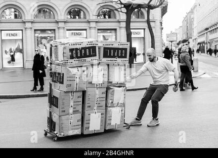 Homme traînant une palette contenant des boîtes de vêtements devant le magasin Fendi à Rome, Italie Banque D'Images