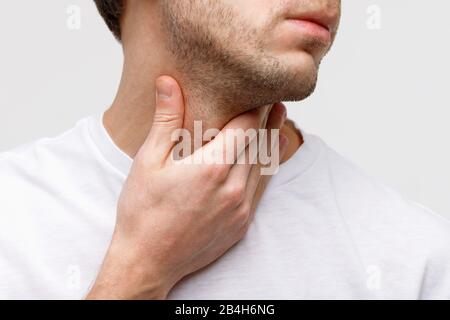 Gros plan sur l'homme malade souffrant de problèmes de gorge, fond gris, isolé. Glande thyroïde, ingestion douloureuse, pharyngite, gonflement laryngé Banque D'Images