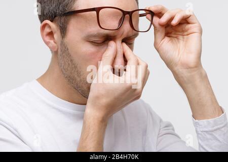 Gros plan portrait de l'homme dans des lunettes frottant ses yeux et pont nez, se sent fatigué après avoir travaillé sur un ordinateur portable, isolé sur fond blanc. Travail Excessif, Banque D'Images