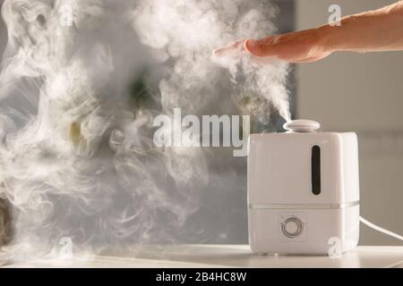 L'homme tient la main sur le diffuseur d'huile d'arôme de vapeur sur la table à la maison, la vapeur de l'humidificateur d'air, l'espace libre. Technologie ultrasonique, augmentation de l'air h Banque D'Images