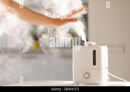 L'homme tient la main sur le diffuseur d'huile d'arôme de vapeur sur la table à la maison, la vapeur de l'humidificateur d'air, l'espace libre. Technologie ultrasonique, augmentation de l'air h Banque D'Images