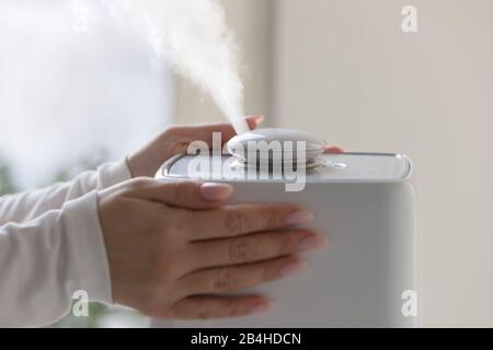 Les mains de la femme touchent et utilisent un diffuseur d'huile aromatique sur la table à la maison, la vapeur provenant de l'humidificateur d'air. Technologie ultrasonique, augmentation de l'humidité de l'air ind Banque D'Images