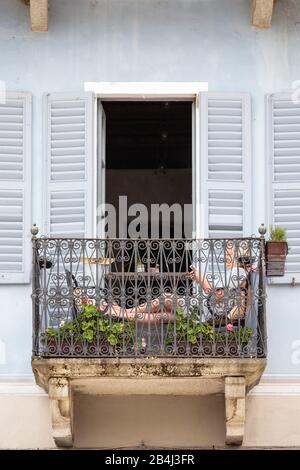Europa, Italien, Piemont, Cannobio. Eine Frau sitzt auf einem kleinen Balkon und lile. Banque D'Images