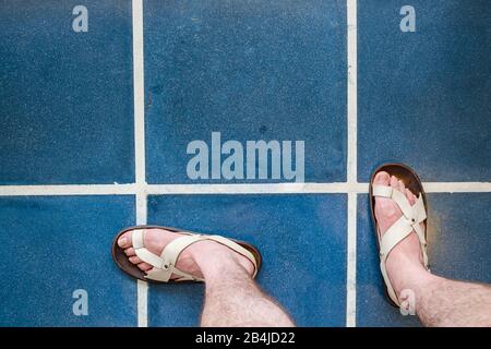 Les pieds dans les sandales sont debout sur des carreaux bleus Banque D'Images