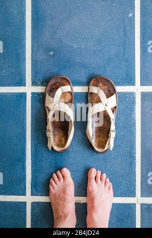 Les pieds dans les sandales sont debout sur des carreaux bleus Banque D'Images