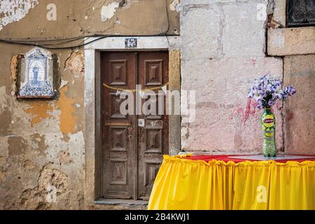 Europe, Portugal, capitale, vieille ville de Lisbonne, Alfama, Rua da Adica, ancienne façade de maison avec porte en bois, table avec fleurs, nappe jaune, bouteille en plastique comme vase, Azulejo Banque D'Images